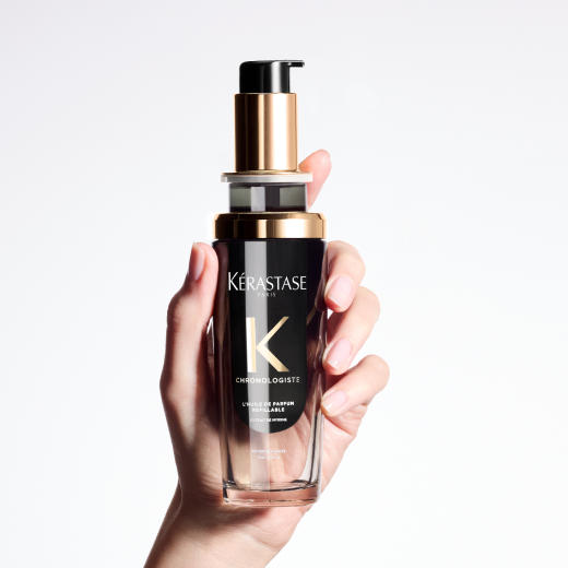  Chronologiste Huile de Parfum hair oil - featuring an artful blend of addictive fragrances mingling cedar, magnolia, and tea rose - is being held between two hands.